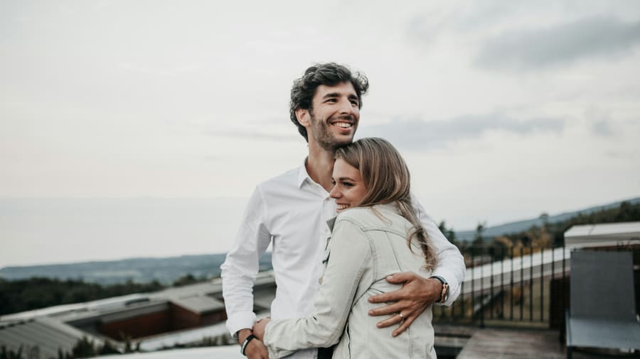 A woman and her companion smiling and looking out over a hazy valley from a hillside terrace.